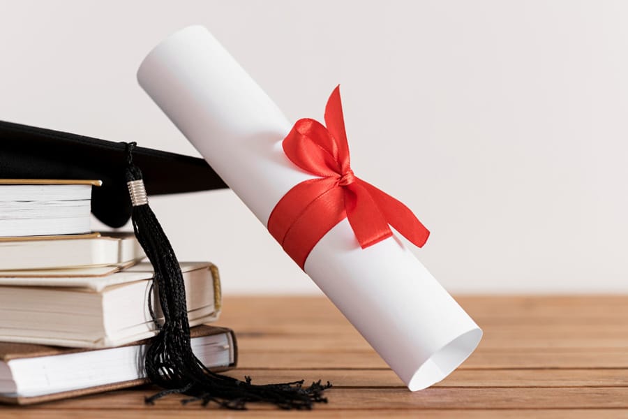 Diploma con lazo rojo junto a birrete y libros representando doble titulación internacional
